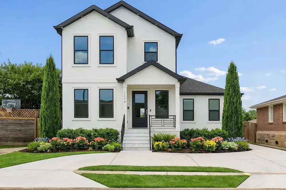 Modern two‑story white home landscaped with Taylor Junipers, Indian Hawthorne, and flowers in Lafayette, LA.
