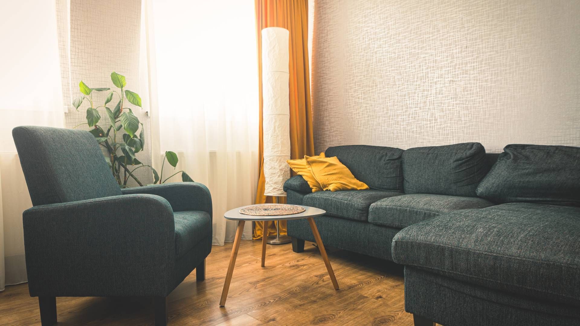 Warm-colored drapes on a window in a living room with dark-colored sofas with mustard yellow pillows