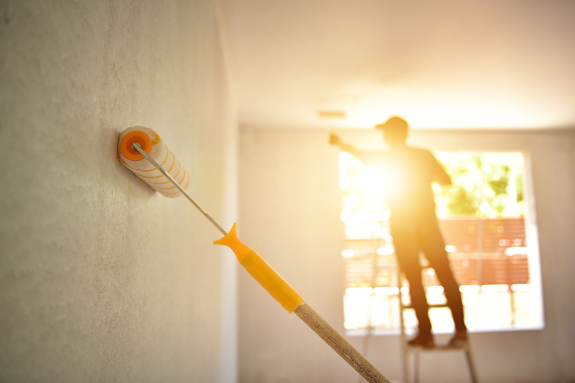 a man on a ladder paints a wall with a roller