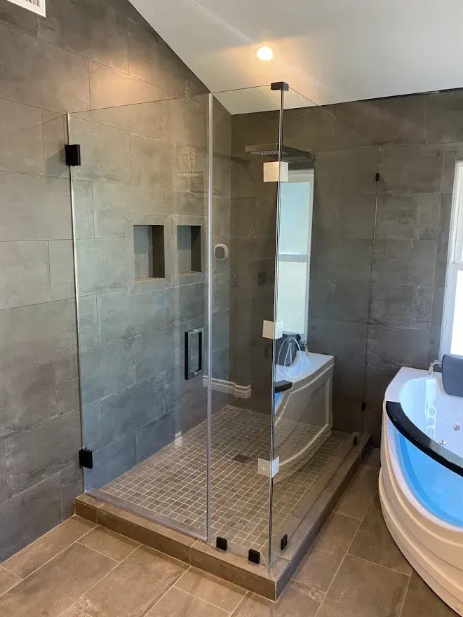 Modern bathroom with a glass shower, grey tile walls, and a jacuzzi tub.