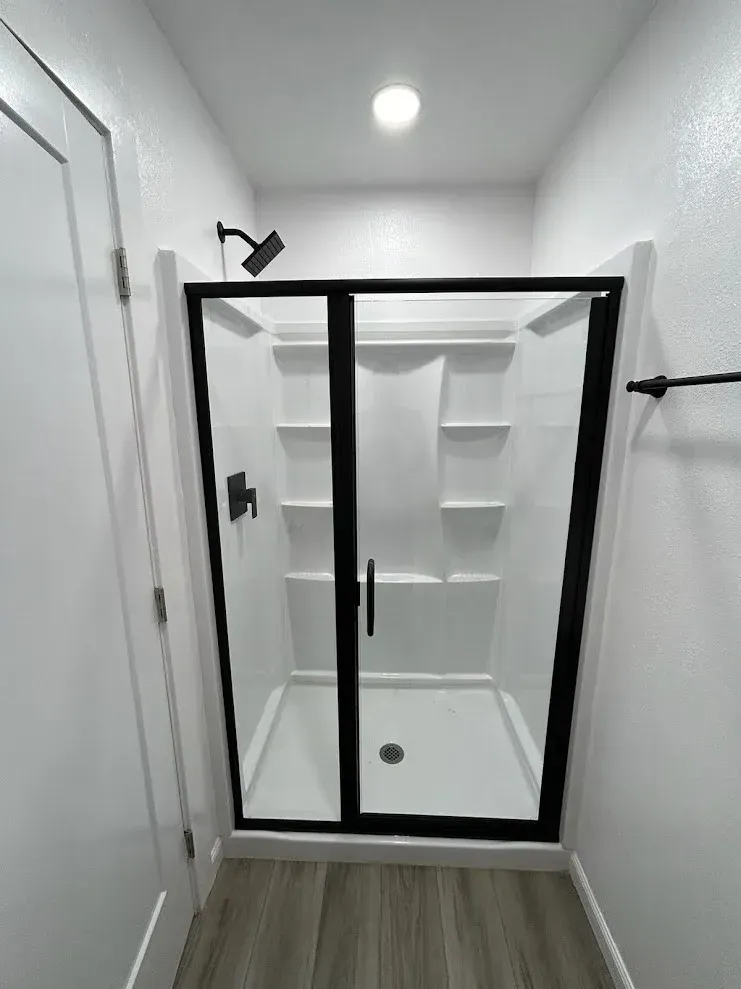 Modern white shower with black trim and fixtures; white walls, wood-look flooring.