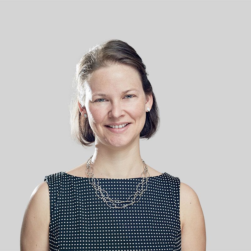 Woman with fair skin, wearing a patterned dress, and silver necklace smiling.