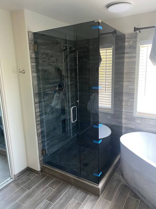 Modern bathroom with glass shower enclosure, gray tiled walls, and a white soaking tub.