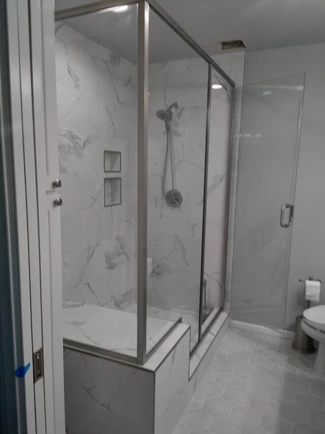 Modern bathroom with a marble-tiled shower, glass doors, and a built-in bench, next to a toilet.