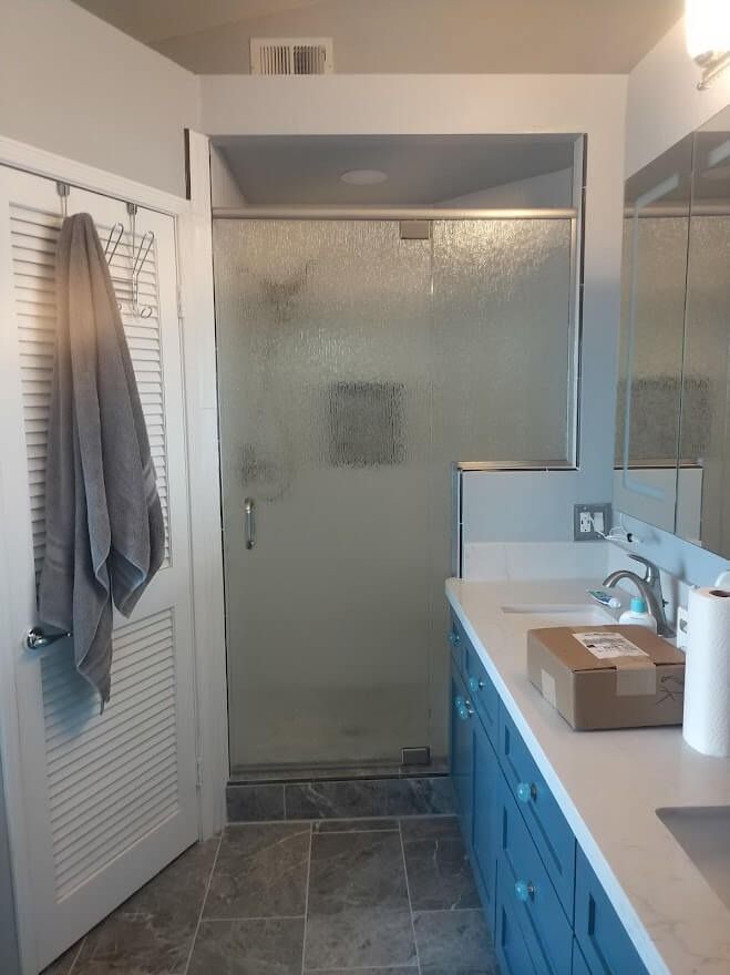 Bathroom with a blue vanity, shower with frosted glass, and a towel hanging on the door.