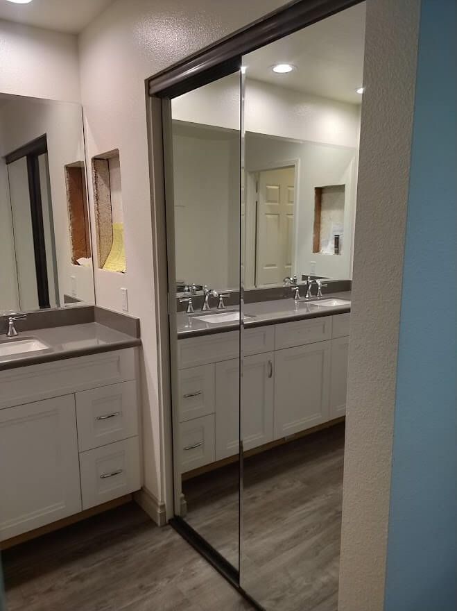 Bathroom with mirrored sliding doors, white cabinets, gray countertops, and wood-look flooring.