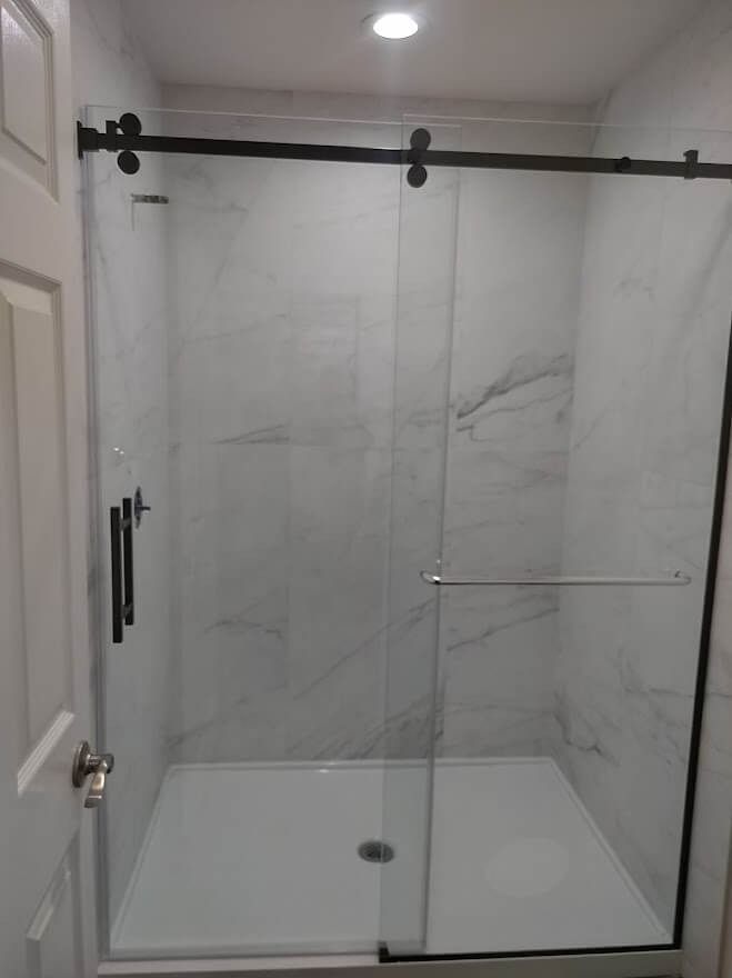 Modern glass shower with black hardware, white walls, and a white shower base.