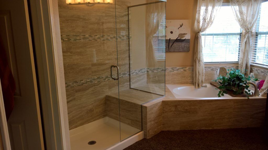 Bathroom with walk-in shower, tub, and window. Beige tile, glass shower door, and floral curtains.