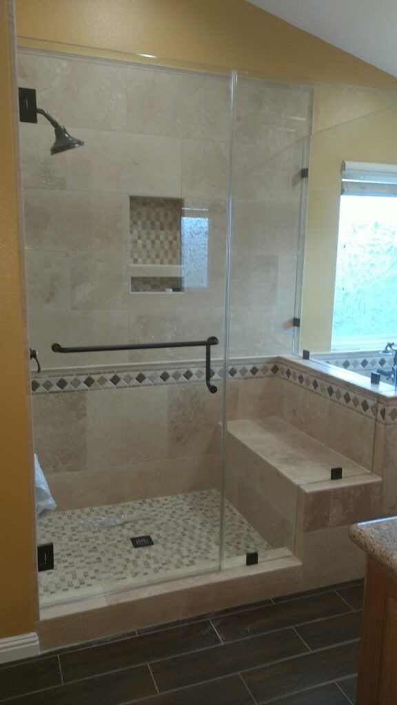 Glass-enclosed shower with a bench and tile, brown and cream colors.
