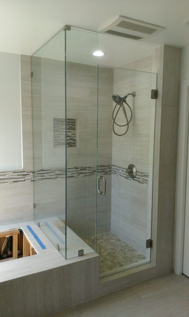 Glass-enclosed shower with pebble floor, tile walls, and a recessed ceiling light in a bathroom setting.