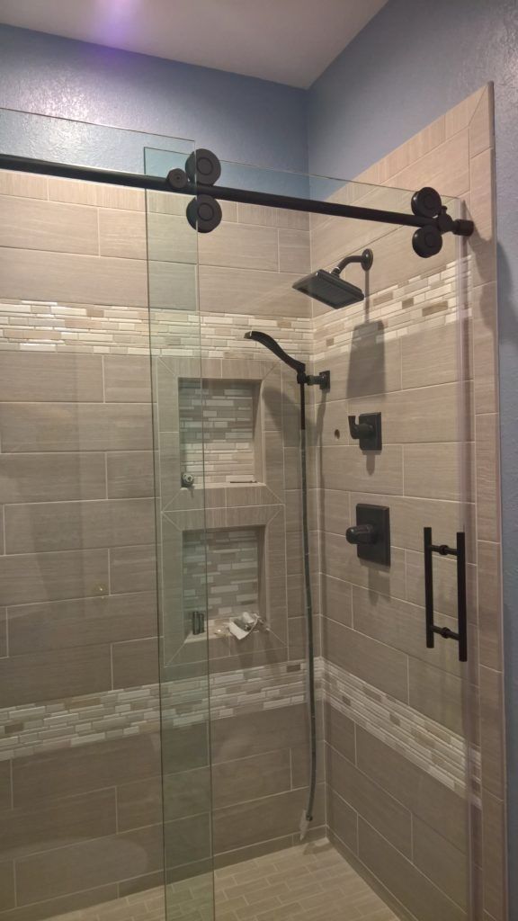 Modern shower with glass door, black fixtures, and built-in shelving. Light gray and blue tile.