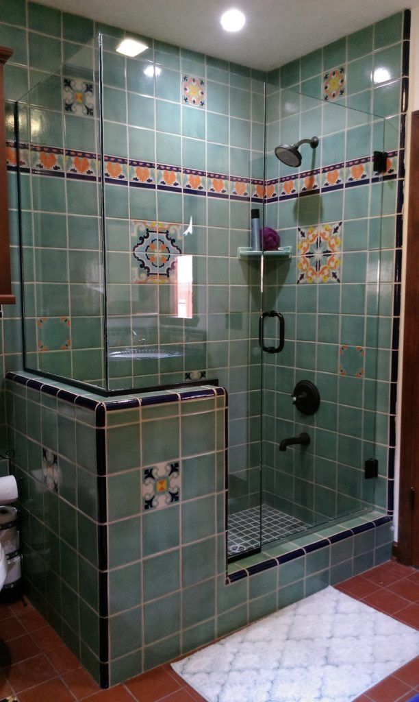 A shower with teal tiles, patterned accents, and glass doors, set in a bathroom with a red floor.