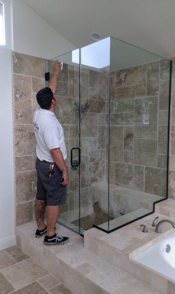 A man installs glass shower enclosure in a bathroom with travertine tile.