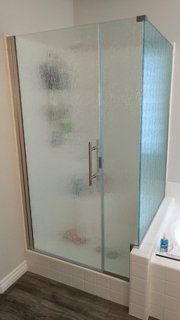Shower stall with frosted glass doors and chrome hardware; white tile and wood-look flooring.