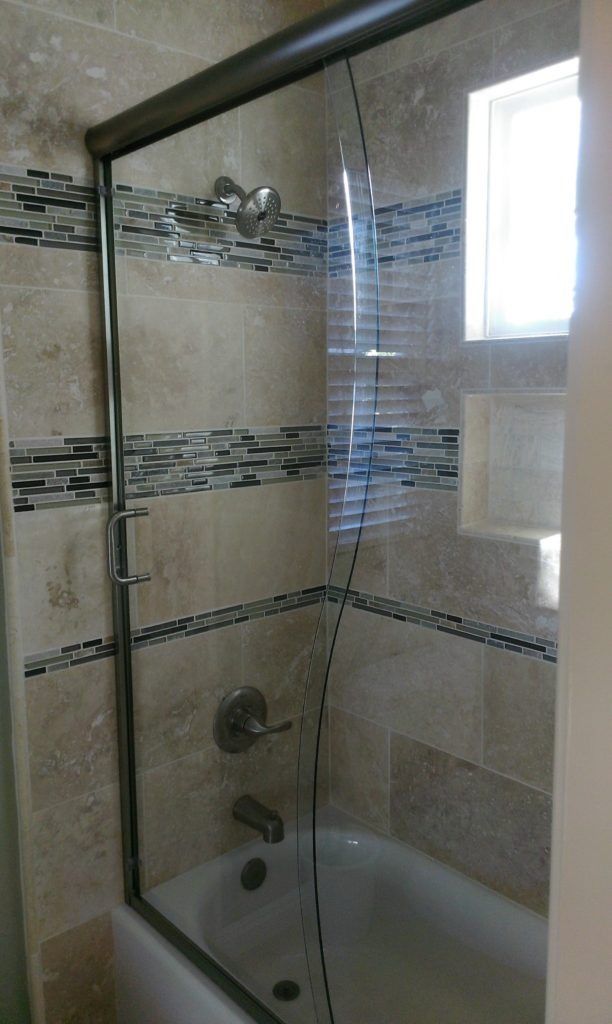 Shower with glass door, beige tile, and decorative mosaic band.  Tub visible.