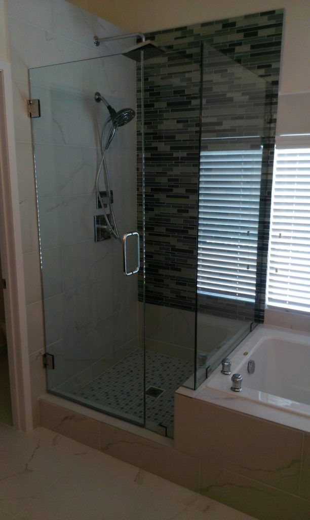 Glass shower enclosure with mosaic tile wall next to a bathtub. Chrome shower fixtures.