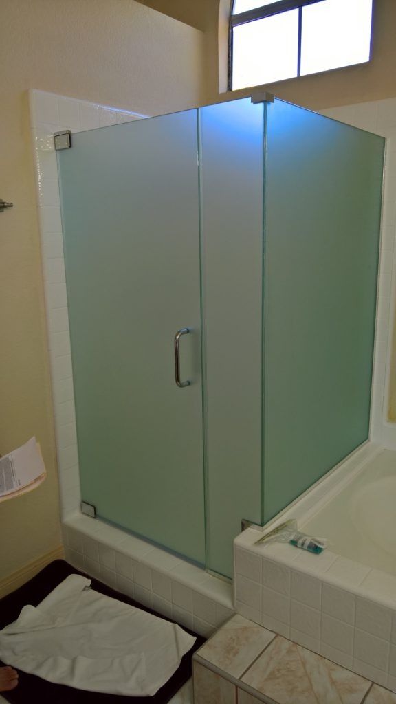 Frosted glass shower stall in a bathroom with a window and a white tub.