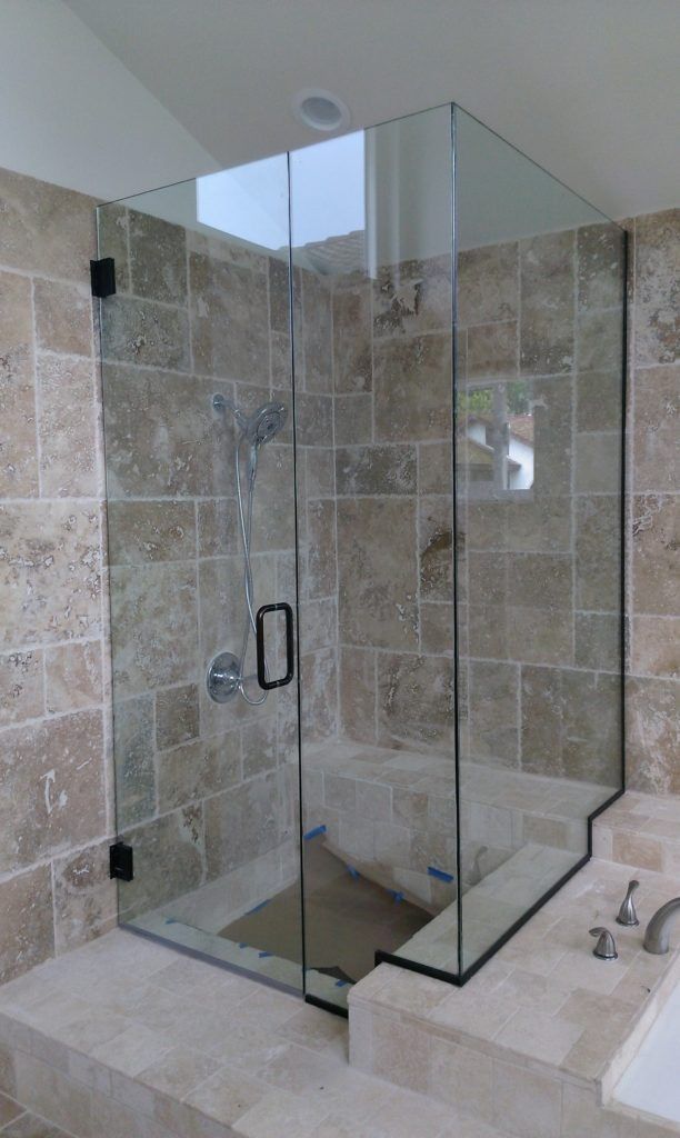 Glass shower enclosure with black hardware, beige tile walls and floor.