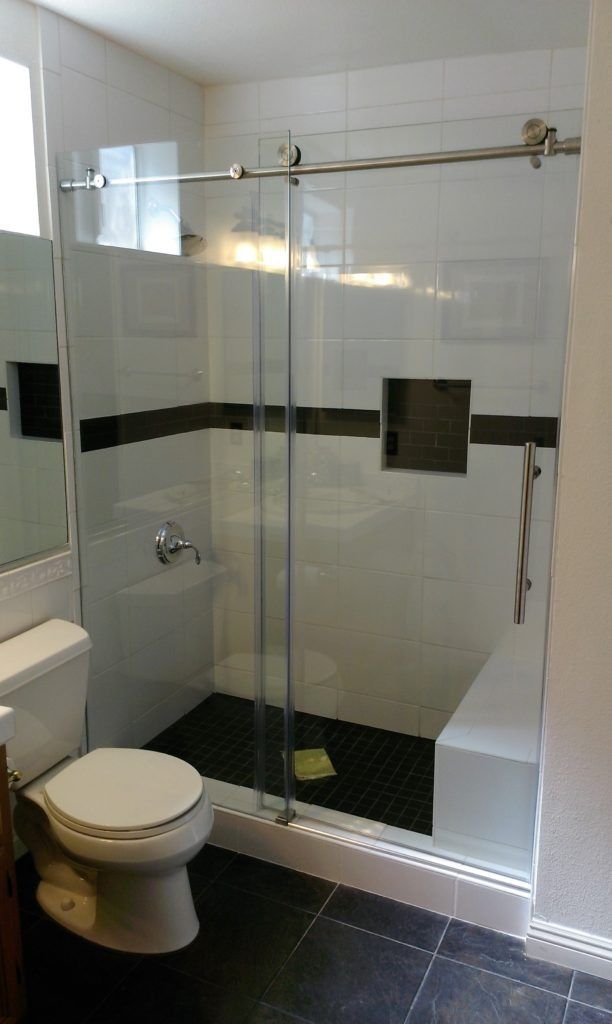 Bathroom with white and black tiled shower, sliding glass door, and a toilet.