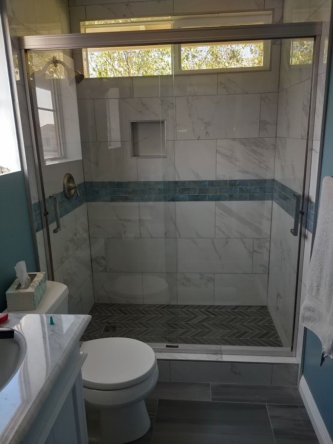 Bathroom with glass shower, white marble tile, teal accent, and toilet.