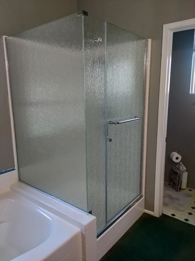Shower stall with textured glass doors, white trim, and a bathtub; bathroom.