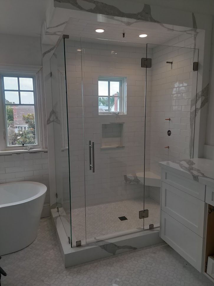 Spacious, modern bathroom with a glass shower enclosure, white tile, and a freestanding tub.