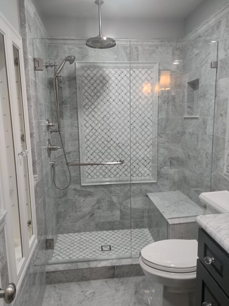 Modern bathroom with glass shower, marble tile, and a built-in bench.
