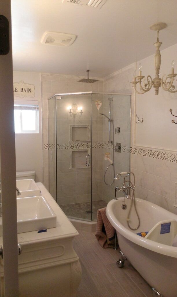 Elegant bathroom with a glass shower, clawfoot tub, chandelier, and double vanity.
