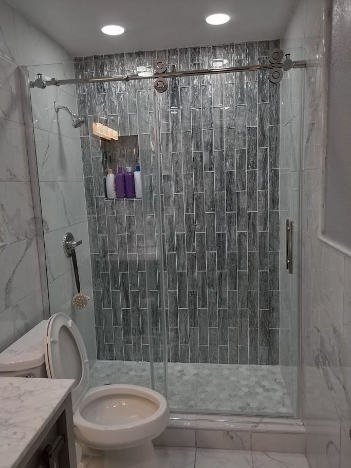 Bathroom with a glass shower, toilet, and marble tile walls. Gray and white color scheme.