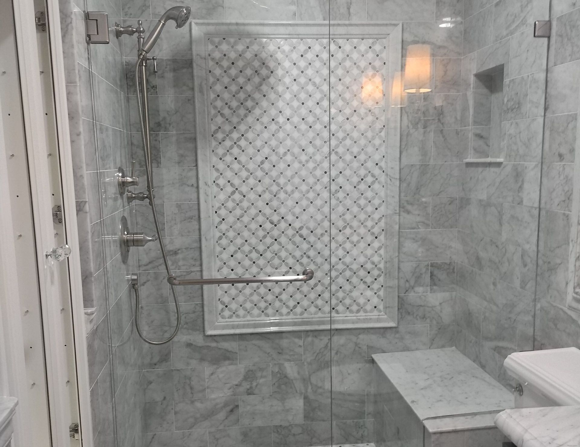 Accessible shower with marble tile, glass door, bench, and handrail.