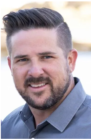 A man with a beard and a gray shirt is smiling for the camera.