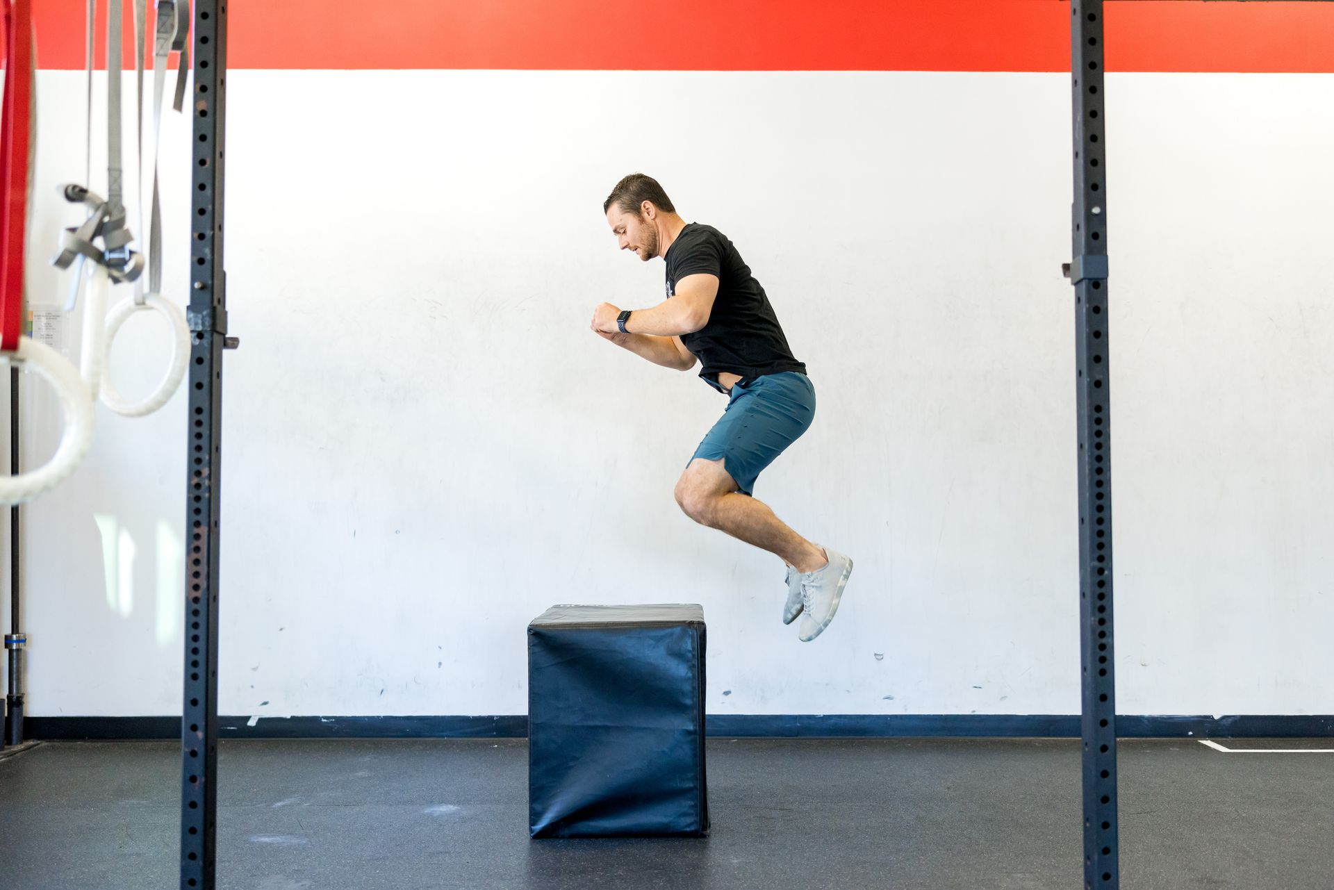 Man in shorts jumps onto a black box in a gym.