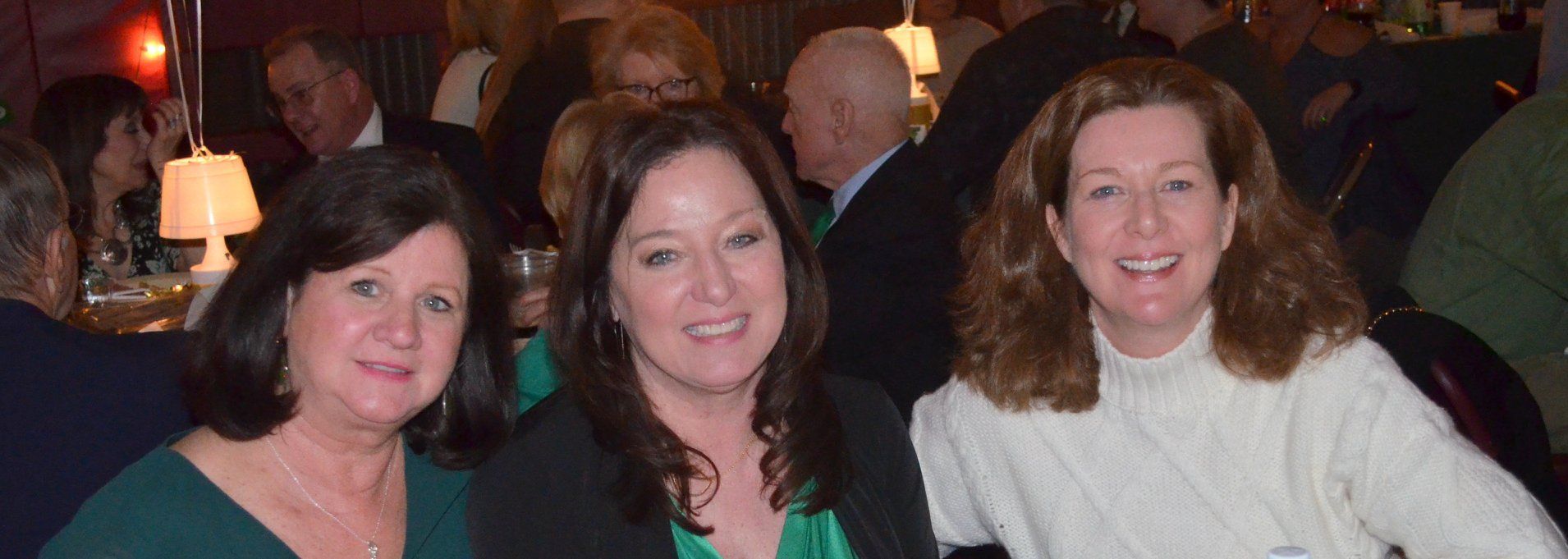 Three women are posing for a picture in a crowded room.