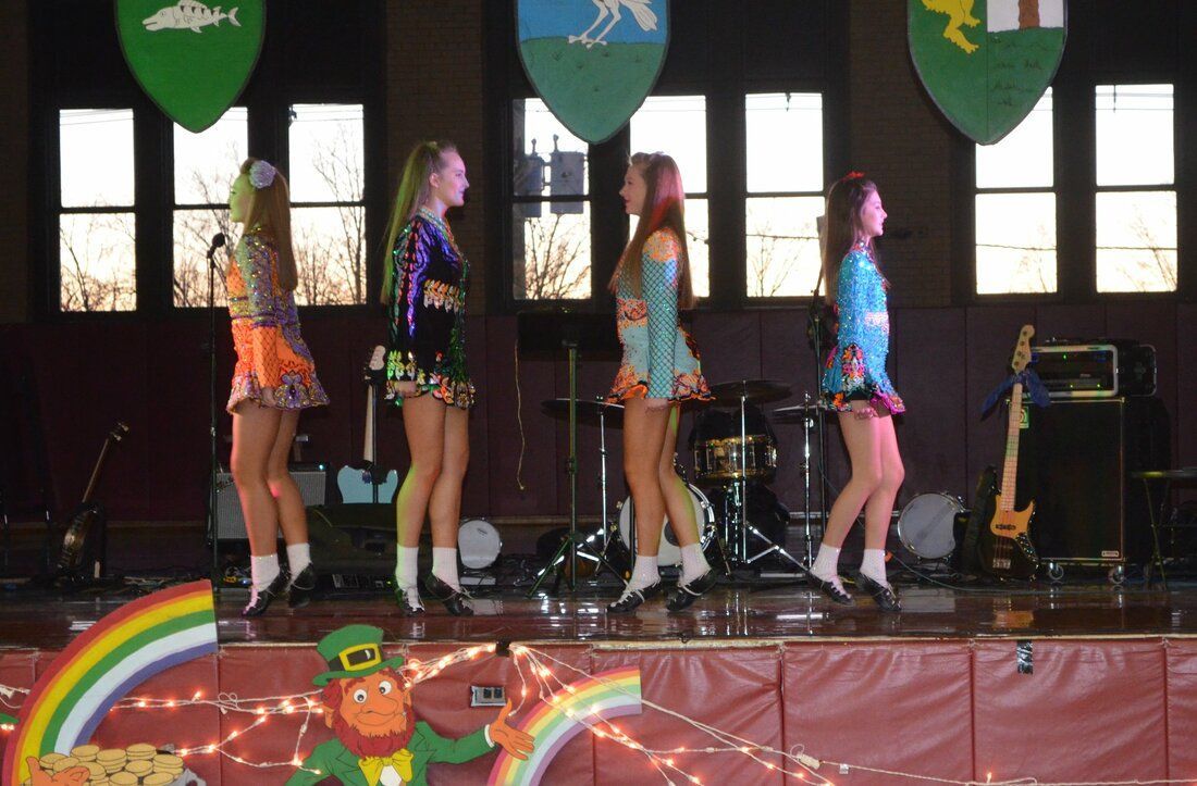 A group of girls are dancing on a stage with a leprechaun in the background