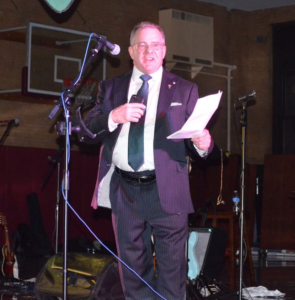 A man in a suit and tie is standing in front of a microphone holding a piece of paper