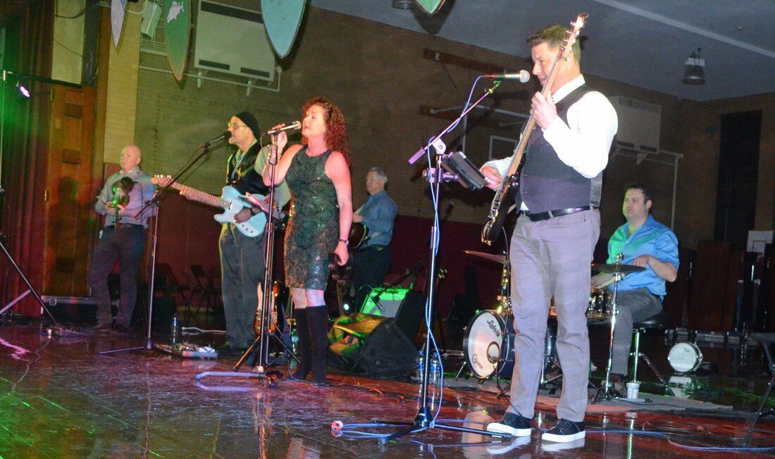 A group of people are standing on a stage playing instruments and singing into microphones.
