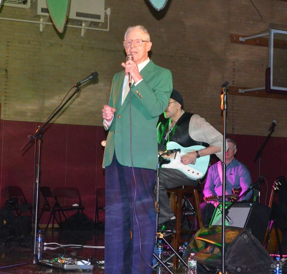 A man in a green jacket is singing into a microphone