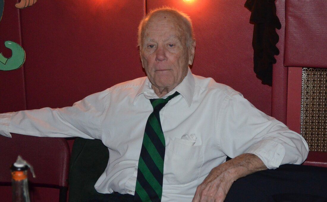 A man in a white shirt and green tie is sitting in a chair