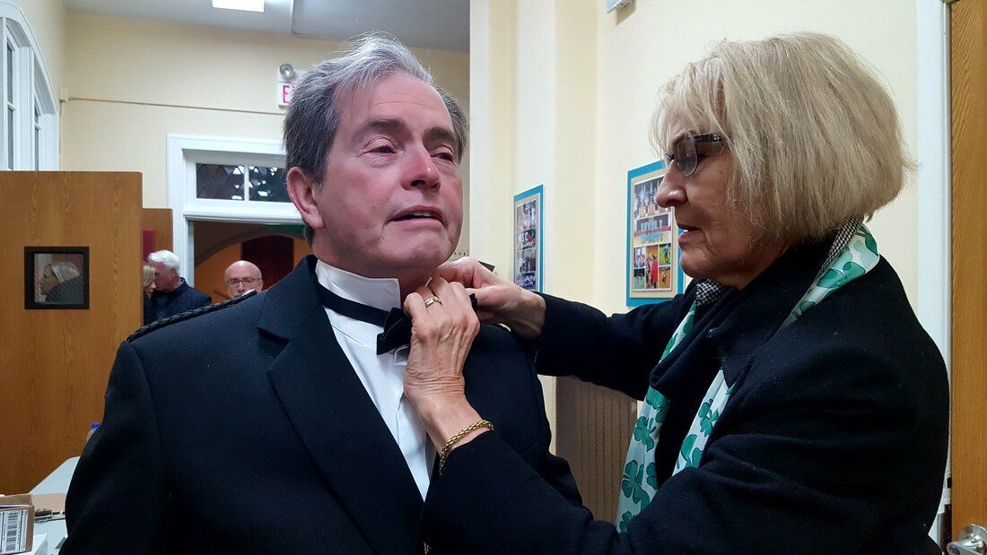 A woman is helping a man tie his bow tie.