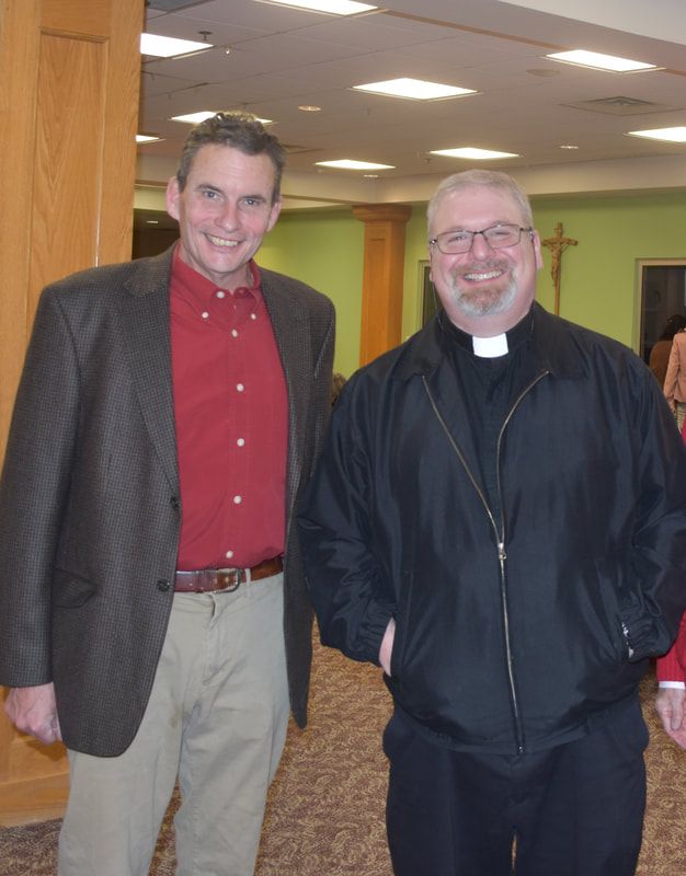 Two men standing next to each other in a room with a cross in the background