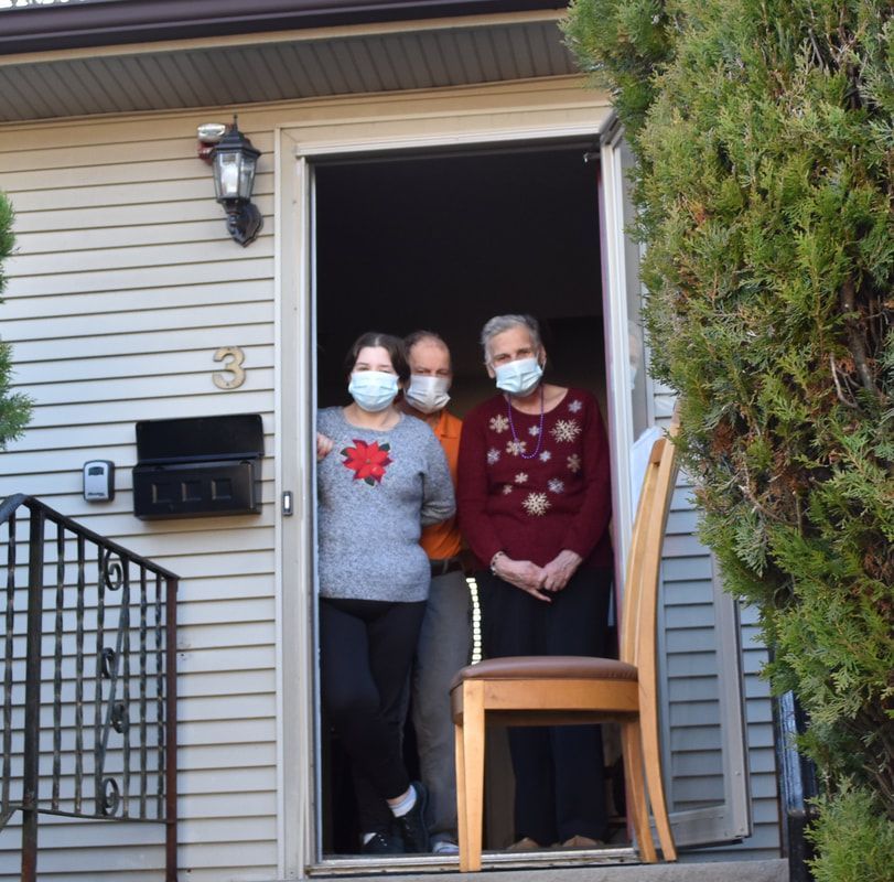Three people wearing face masks are standing in the doorway of a house