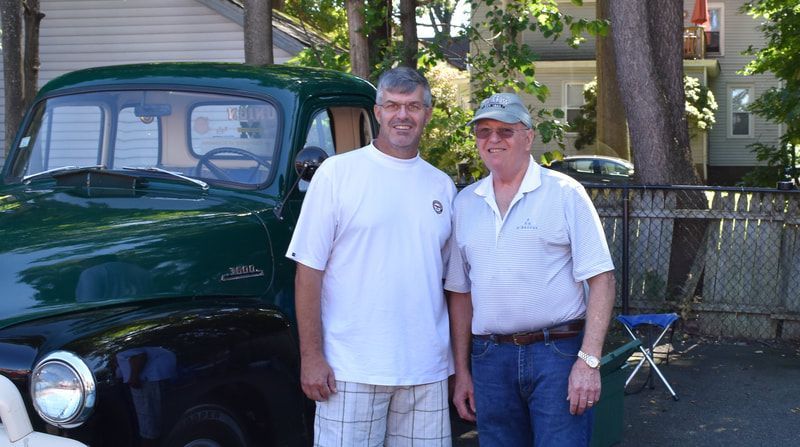 Two men are posing for a picture in front of a green truck