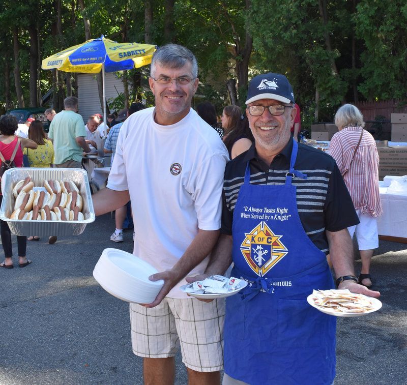 Two men standing next to each other holding plates of food