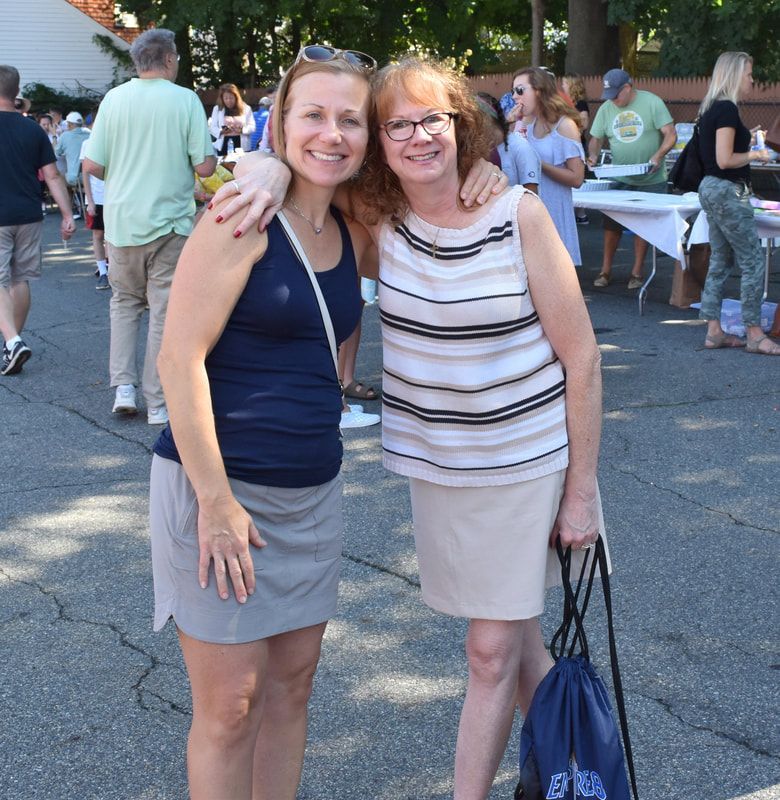 Two women posing for a picture with one holding a blue bag that says ' eku ' on it