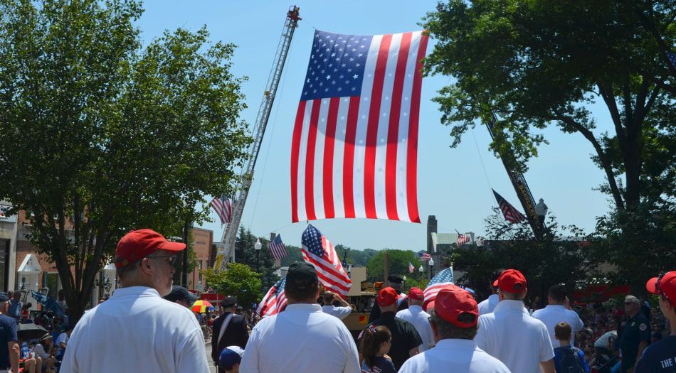 A large american flag is flying over a crowd of people