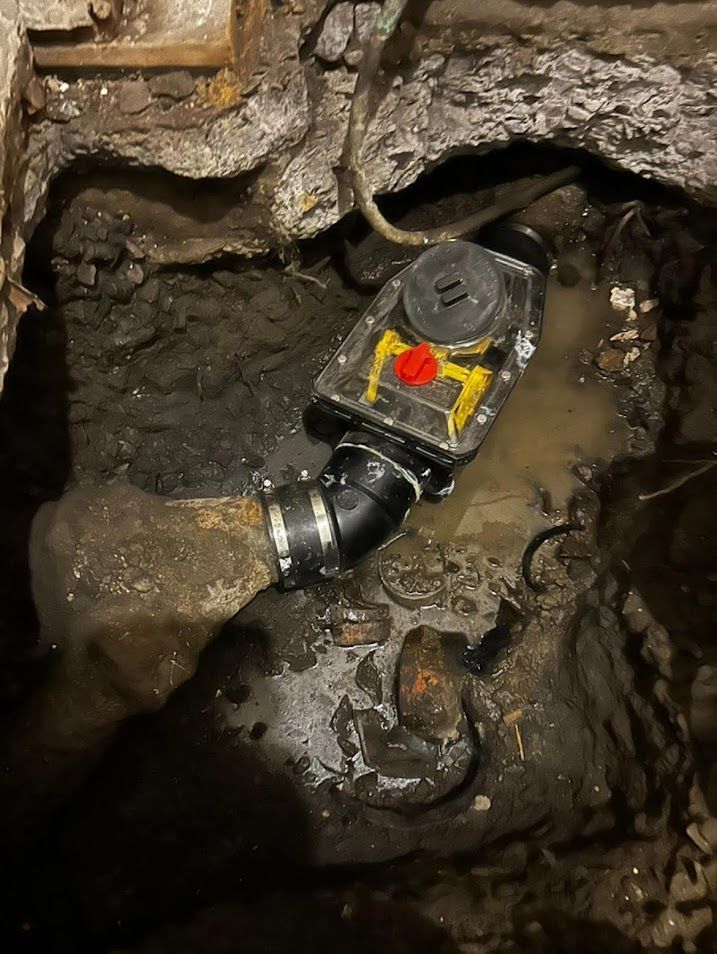 Une pompe de puisard installée dans une zone boueuse et excavée, avec des tuyaux et des câbles apparents.