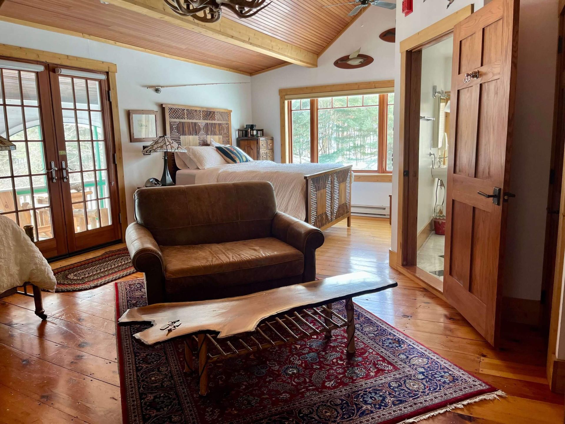 Cozy bedroom with bed, armchair, wooden coffee table, rug, and French doors to a porch.