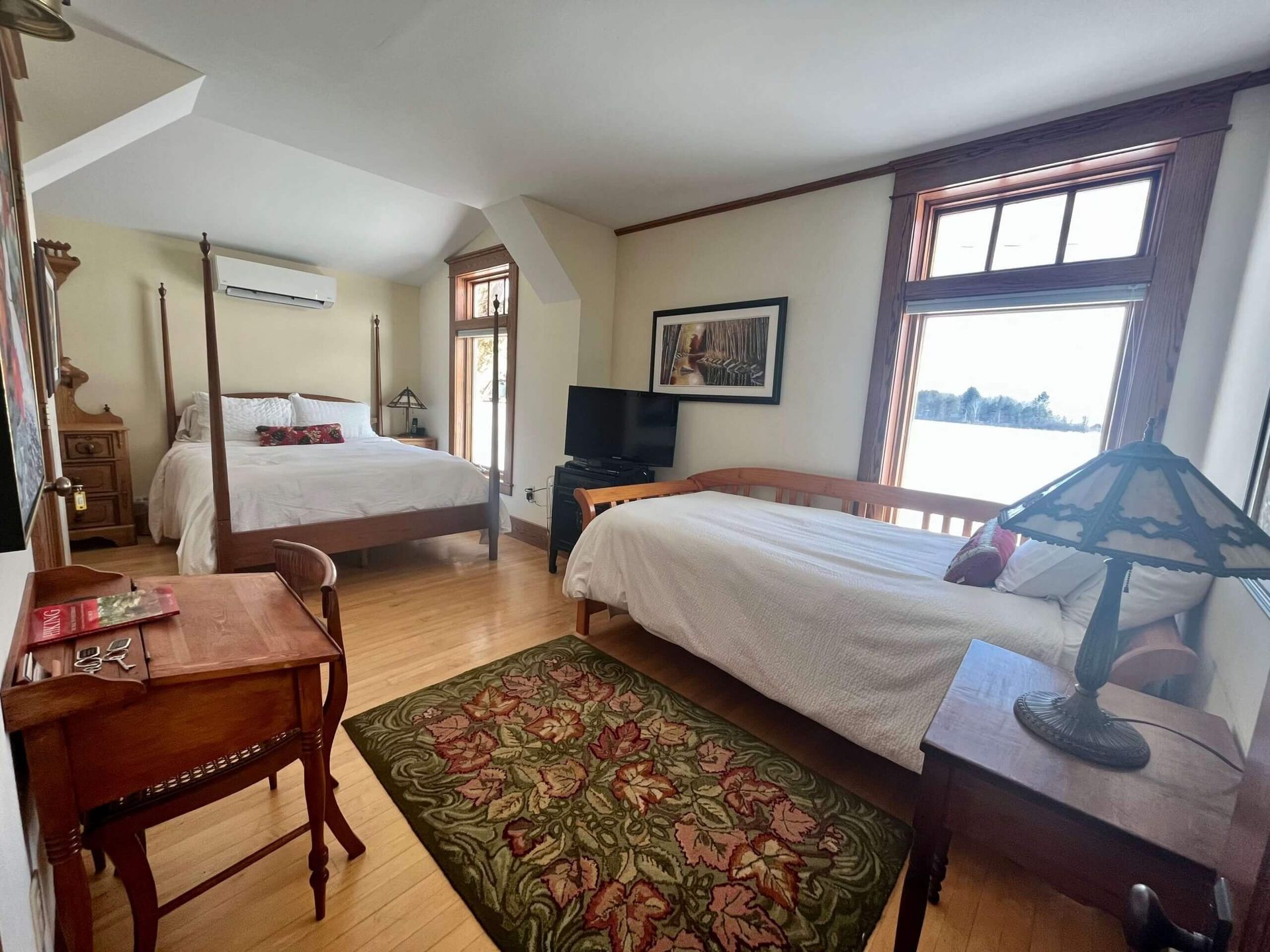 Bedroom with a four-poster bed, twin bed, desk, and decorative rug.  Large window overlooks water.