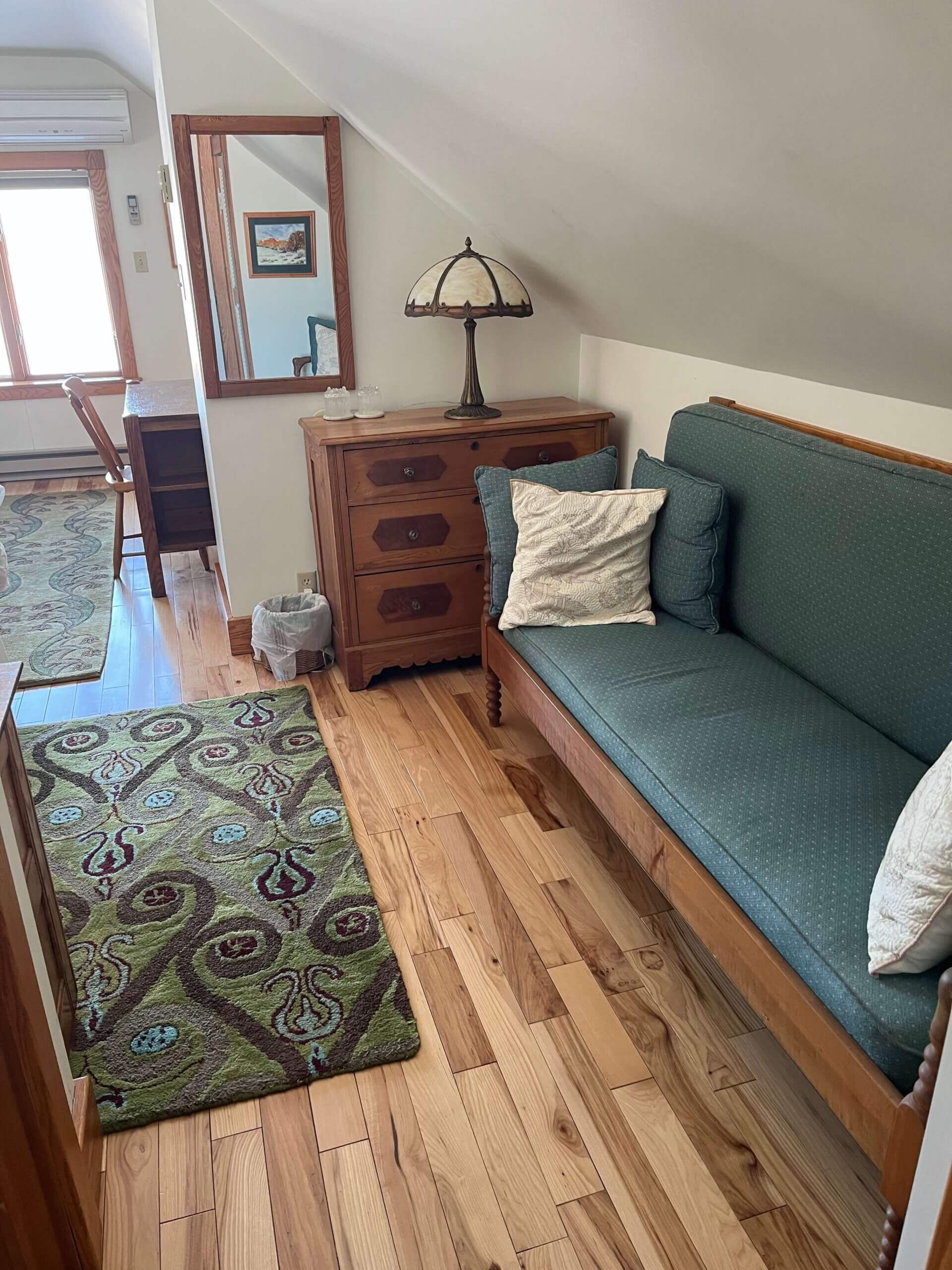 Small room with green sofa, wooden dresser, ornate rug, and sloped ceiling.