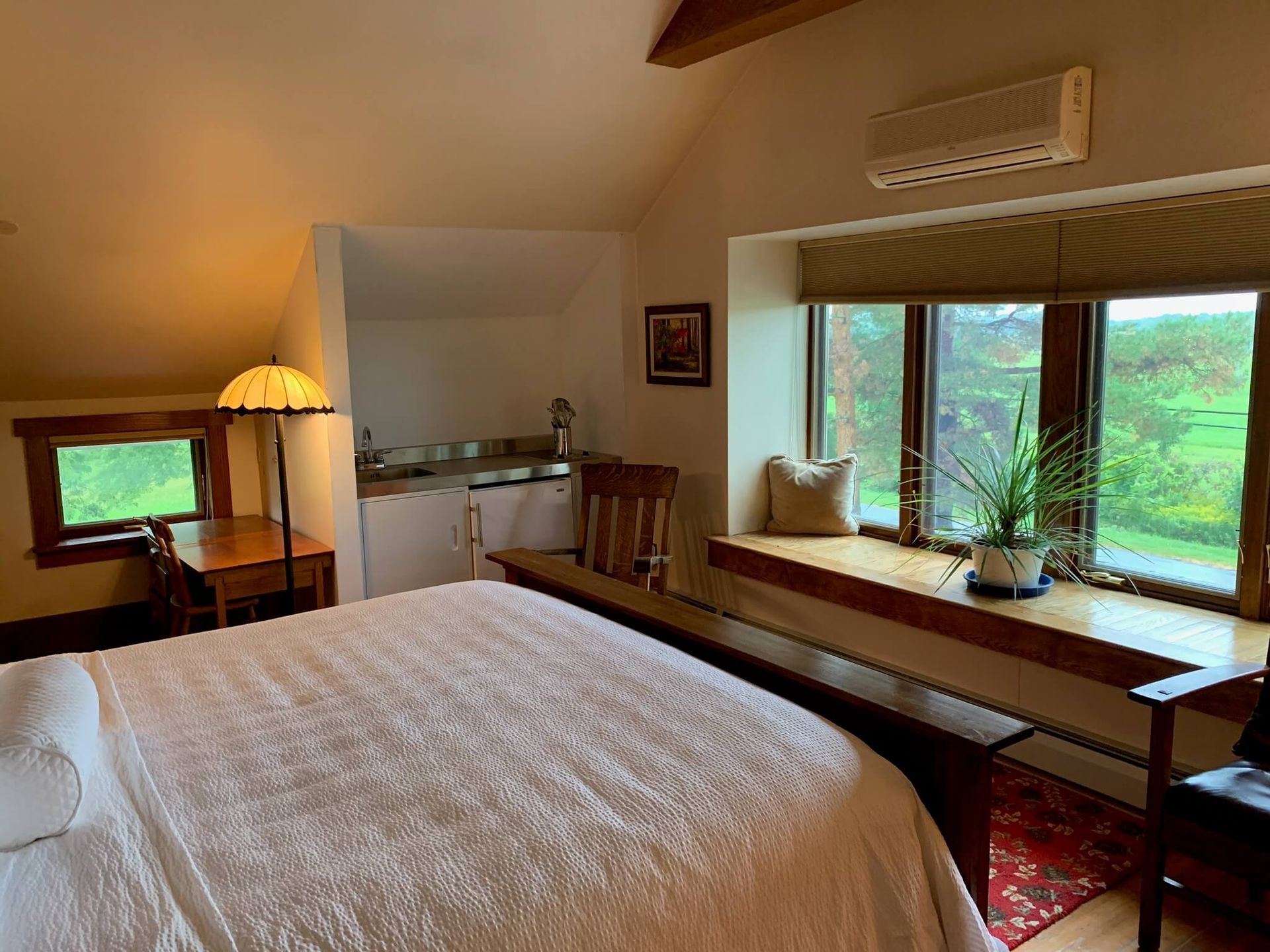 Bedroom with bed, desk, window seat, and small sink.